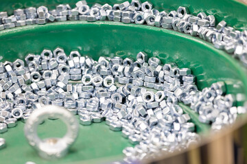 Hex Nuts on Vibratory Feeder Bowl in Factory. Shiny hexagonal metal nuts being aligned and sorted on a green vibratory feeder in an automated industrial environment. Selected focus