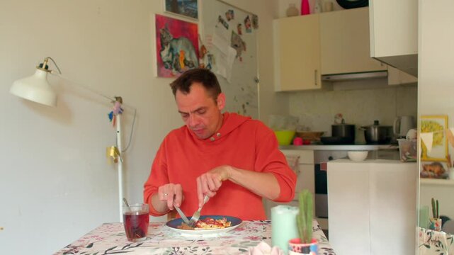 white man eating, man in red hoodie enjoying meal, focused man with red hoodie savoring juice and meal, white man in red hoodie peacefully enjoying his lunch with attentive posture and warm lighting