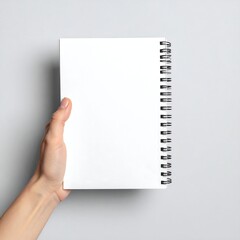 A hand holding a blank notebook with a spiral binding