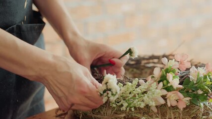 Close up of female hands arranging small white flowers into handmade floral wreath with twigs and hay, highlighting delicate craftsmanship, creativity, and rustic decorative design process in natural - Powered by Adobe