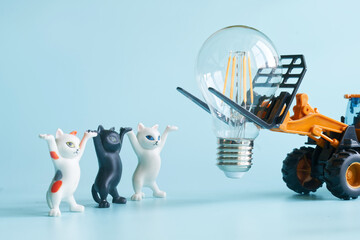 Toy forklift and cute toy kittens dressed as electricians prepare to mount an energy-saving LED bulb in a playful scene about electrification and conservation. Photo