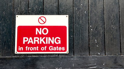 No Parking in front of Gates warning sign with a prohibition symbol mounted on dark, distressed...