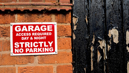 Strictly No Parking warning sign for garage access day and night, displayed on a red brick wall...