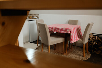 Rustic dining setup with beige chairs and red checkered tablecloth in a small kitchen corner. Ideal for home, lifestyle, and hospitality concepts