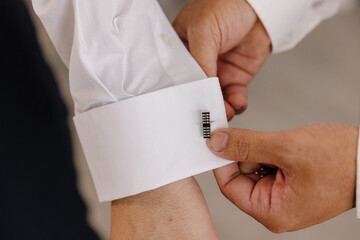 Close-up of a man securing an elegant silver bar-style cufflink on the pristine white shirt cuff of the groom
