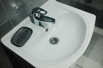 White ceramic sink with chrome faucet and soap dish on tiled wall background. Perfect for hygiene,...