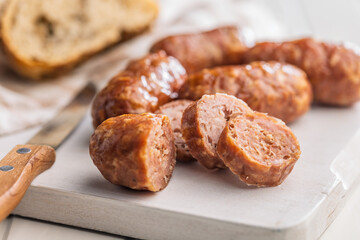 Photo of roasted italian sausage salsiccia on cutting board on white table.