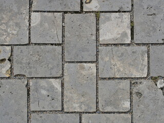 Gray natural stone paving with block-bonded joints, cracks, and moss. A detailed surface. Ideal as a texture. Copyspace