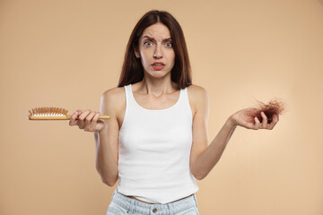 Woman with brush and lost hair on beige background. Alopecia problem