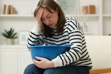 Woman with basin suffering from nausea in armchair at home