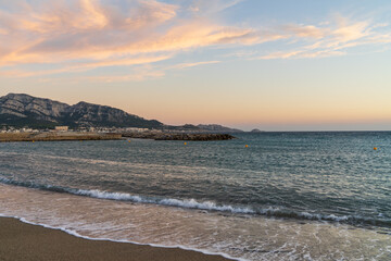 Serene sunset over the Mediterranean Sea from a sandy beach in Marseille, with the stunning Calanques mountains in view, France.