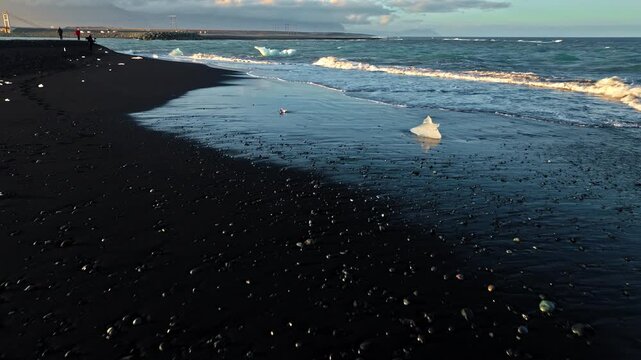 Aerial view of glacial ice on black beach Jokulsarlon Iceland. Waves gently wash around the sparkling ice creating a dramatic contrast.