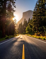 Fototapeta premium A sunlit road curves through a towering forest toward a rocky mountain