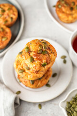 Savory zucchini muffins with ham, cheese and seeds in stack on a plate on white kitchen table background. Healthy and quick morning breakfast