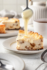 A piece of homemade cottage cheese casserole with raisins, process of pouring condensed milk on top. Baked cheesecake for breakfast on white table background