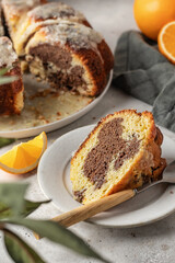 Piece of orange and chocolate marble bundt cake with sugar icing close up. Fruity citrus dessert on light gray kitchen background