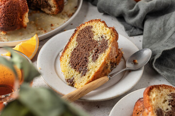 Piece of orange and chocolate marble bundt cake with sugar icing close up. Fruity citrus dessert on light gray kitchen background