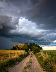 Dirt path through fields toward dark, stormy clouds overhead