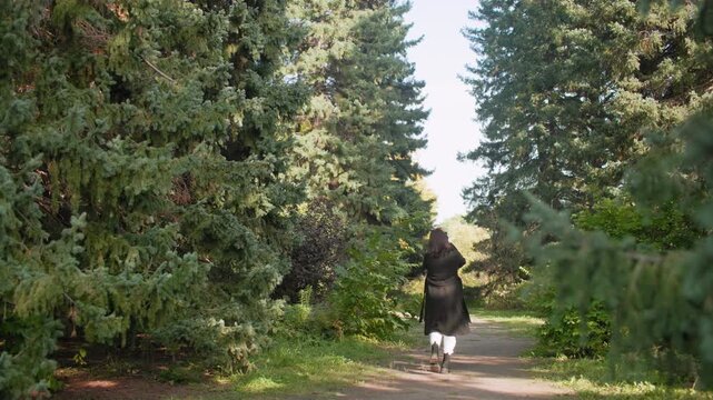 long shot nature lover in long winter coat strolling through arboretum, holding phone and raising it to take shots among tall pines, peaceful walk capturing greenery during relaxed autumn day - Powered by Adobe