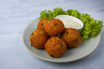 Fried potato balls served on a plate with sauce and a lettuce leaf
