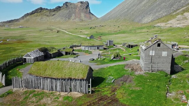 Viking Village and Vestrahorn peaks Stokksnes Iceland. Drone reveals wooden huts in a green valley under sharp mountain spires.