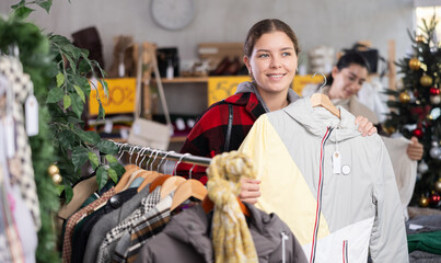 Young woman standing choosing a down jacket in a Christmas shop. Buyer at the sale of winter outerwear before the new year