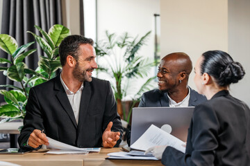 Business professionals engaged in a lively discussion at a modern office table, surrounded by greenery, showcasing collaboration and teamwork in a corporate environment