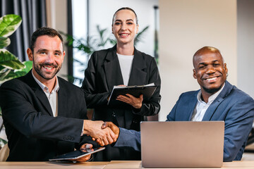 Business professionals engaged in a handshake, with a smiling woman holding a clipboard, showcasing...
