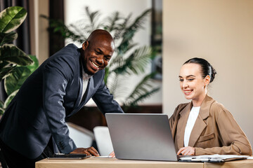 Businessman and businesswoman engaged in a collaborative meeting at a modern office, discussing ideas while working on a laptop, showcasing teamwork and professionalism