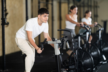 Obraz premium Young guy in sportswear training on exercise bike in gym