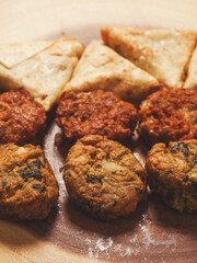Close up of Indian style starter food selection of samosa, bhajis and pakoras on wooden board. Party sharing finger food variety made from fine products and aromatic spices. Special orient vibe.
