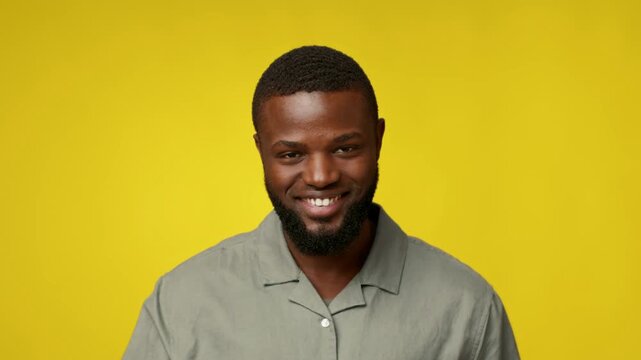 A stylish millennial African American man stands confidently, smiling at the camera. He touches his temple, suggesting thoughtfulness or inspiration, with a cheerful yellow background.