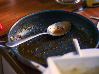 A dirty pan with a spoon in it. The pan is full of food grease and the spoon is in the middle of it. Cooking area.