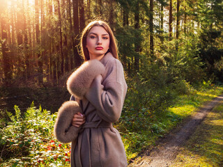Stunning young girl in stylish clothes on a walk in a forest park. Selective focus. Model wearing glamour warm jacket on a sunny day. Enthusiastic and confident young woman enjoy nature.