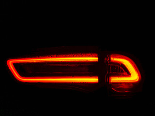 A car's tail light is lit up in red. The light is bright and stands out against the dark background. Modern any shape vehicle rear and front illumination technology.