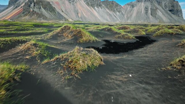 Drone flying over dunes at Vestrahorn Stokksnes Iceland. Smooth motion captures sunlight over black sand patterns and green grass mounds.