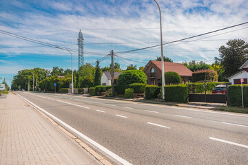 Rural street in a Belgian village, with traditional houses and high-voltage towers in the background