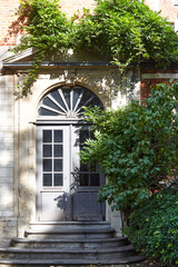 Close-up view of ornate door framed by lush greenery, showcasing intricate architectural details and textures, creating serene and inviting atmosphere with natural elements surrounding the entrance