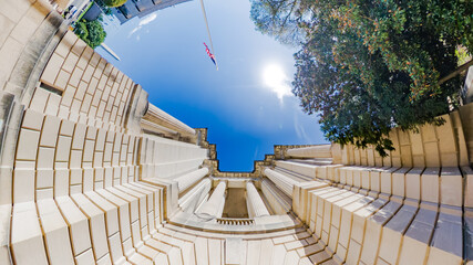 Dramatic architectural composition from the base of a Washington, DC landmark. Featuring columns, flag, and a distant view of the Washington Monument.
