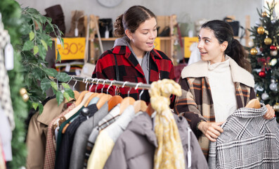 Two cheerful girls looking for winter outwear in retail outlet during X-mas sell-out season