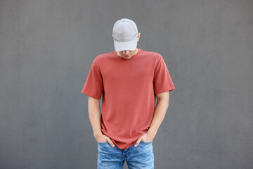 Young man wearing blank red t-shirt near grey wall. Mockup for design