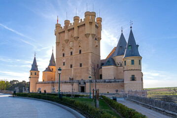Fototapeta premium The iconic Alcázar de Segovia castle's imposing keep and whimsical turrets are almost in silhouette against the bright, late afternoon sky, bathed in warm sunset light