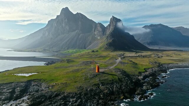 Drone orbit of lighthouse Hvalnes Iceland. The camera circles the orange tower overlooking vast ocean and distant peaks.