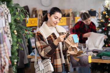 Uncertain young Armenian girl choosing convenient bra in clothing shop during Christmas sale