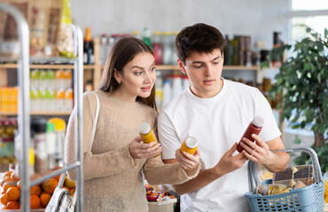 Couple young man and woman buyers chooses red and yellow smoothie in bottle in grocery store