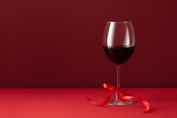 Elegant still life composition with a glass of red wine and red satin ribbon on a red background