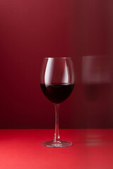 Minimal still life of red wine glass on a deep red background with soft reflections