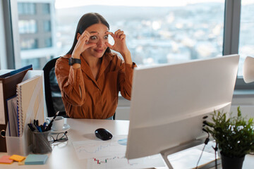 Sleepy businesswoman trying to stay awake keeping her eyes opened with fingers, looking at desktop...