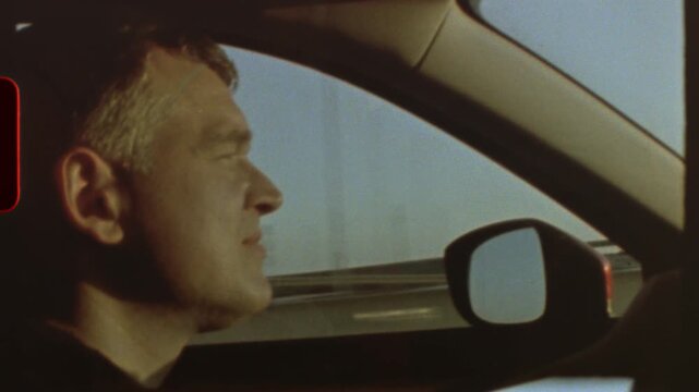 Filmed on super 8 film Middle aged driver navigating highway lane, vintage 8mm film aesthetic capturing side profile through car window with nostalgic grainy texture and cinematic movement