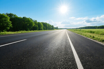 Obraz premium A sunny asphalt road stretches ahead with green trees lining both sides under a clear blue sky.
